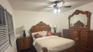 Una camera da letto con un letto in legno, una ventola a soffitto, una cassettiera, uno specchio e una finestra con persiane.