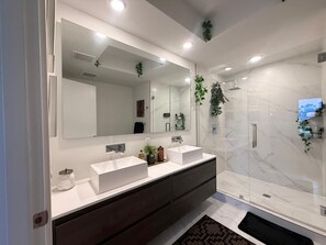 A modern bathroom with a large mirror, two sinks, a shower, and decorative plants. - Cozy 1-bedroom condo in tranquil Pompano Beach with AC (Pompano Beach)