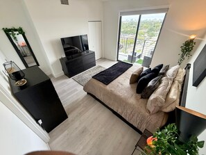 A modern bedroom with a bed, a TV, a wardrobe, and a balcony with a city view. - Cozy 1-bedroom condo in tranquil Pompano Beach with AC (Pompano Beach)