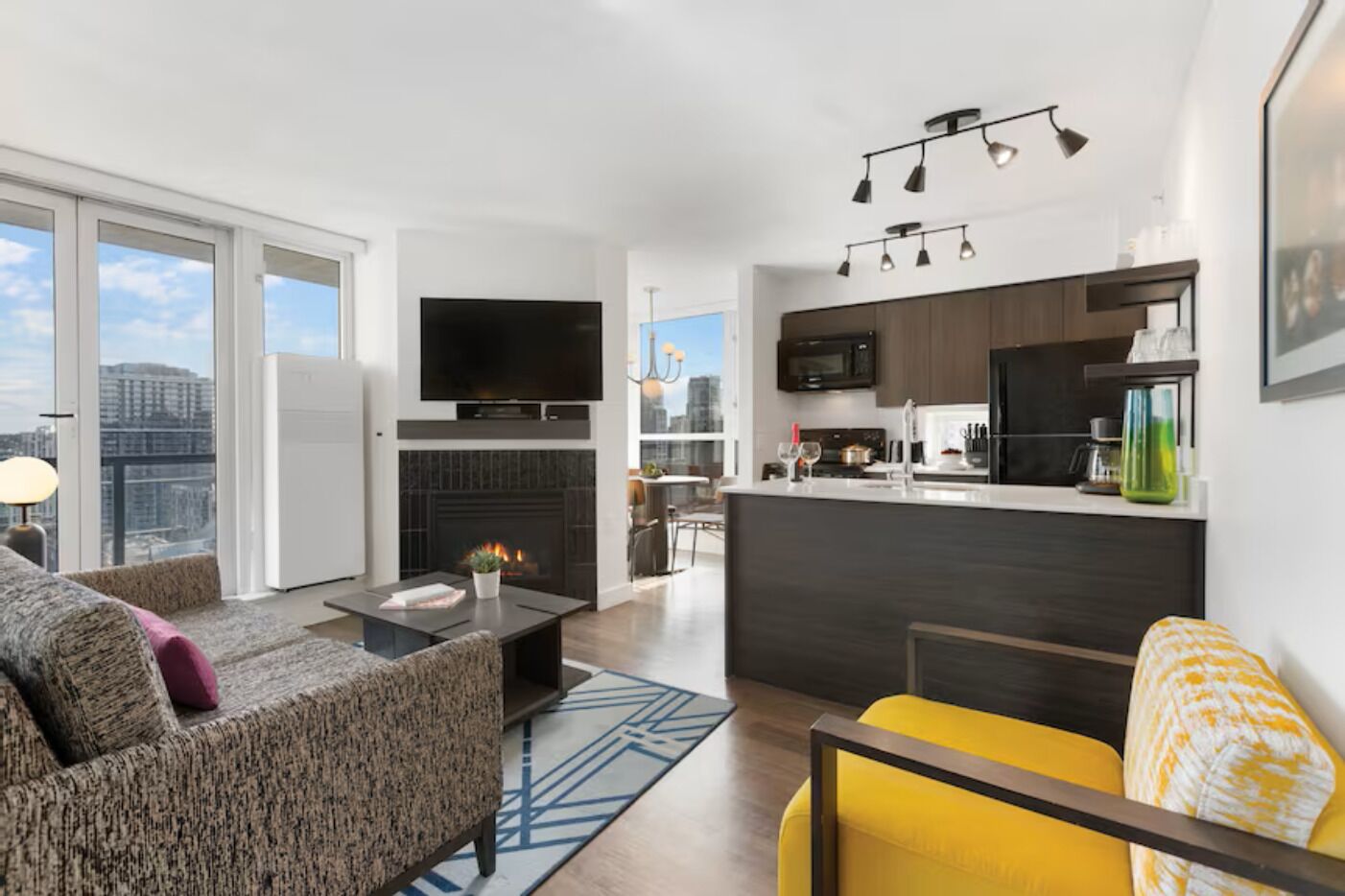 Un apartamento moderno con sala de estar, cocina y comedor, que cuenta con chimenea, televisor de pantalla plana y vistas a la ciudad.