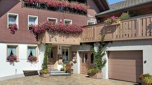 A two-story building with a balcony, a garage, and a small entrance. - Haus Schmid - Apartment Dompfaff with Mountain View, East Balcony, Wi-Fi (Lenzkirch)