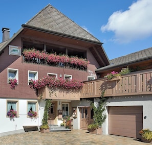 Een gebouw met twee verdiepingen, een balkon, een garage en een kleine ingang.