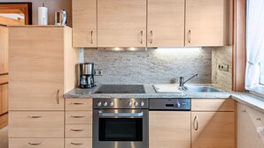 A modern kitchen with wooden cabinets, a stainless steel oven, a coffee maker, and a sink. - Haus Schmid - Apartment Dompfaff with Mountain View, East Balcony, Wi-Fi (Lenzkirch)