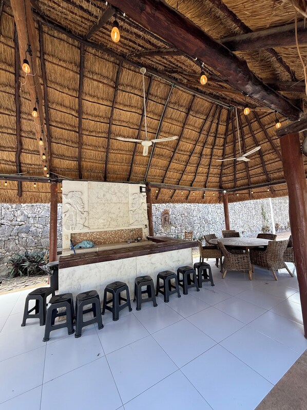 Un espace ext érieur aménagé avec un toit de chaume, des murs en pierre et un bar central doté de tabourets.