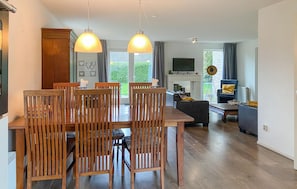 A dining area with wooden chairs and a table, a living room with a sofa and TV, and a view of greenery outside. - 3 bedroom nice home in Zeewolde (Zeewolde)