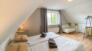 Una habitación con dos camas, una mesita con una lámpara, una silla, un radiador y una ventana con cortinas.