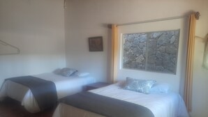 Dos camas individuales con cabeceros, una obra de arte de piedra sobre una ventana y suelo de madera.