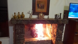 Una chimenea de piedra con un reloj encima, un televisor a la derecha y un cuadro en la pared.