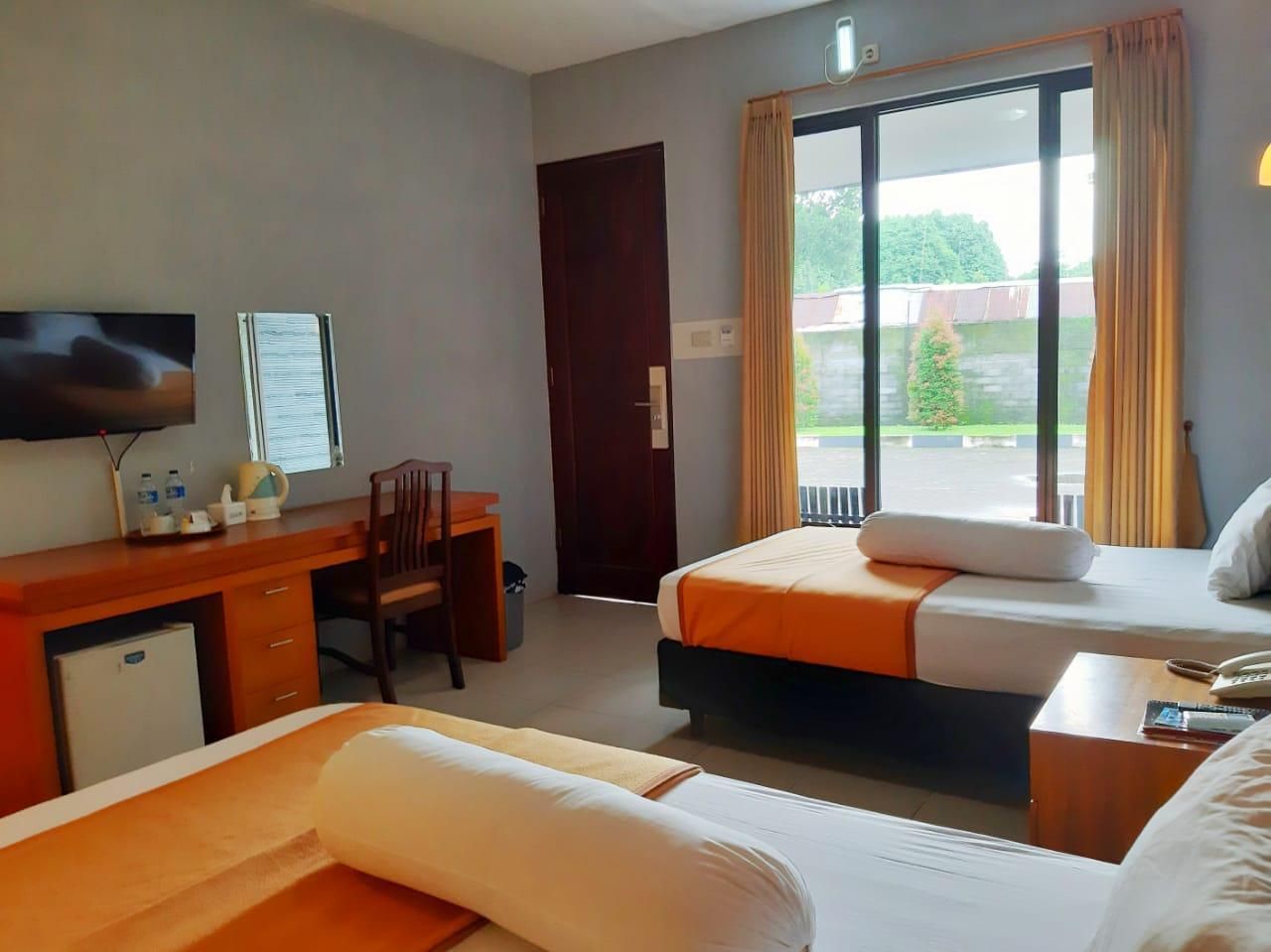 A hotel room with two beds, a desk, a chair, a television, and a sliding glass door to the outside.