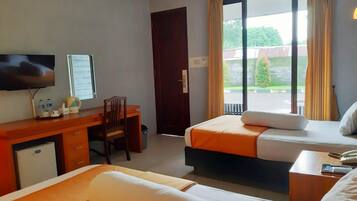 A hotel room with two beds, a desk, a chair, a television, and a sliding glass door to the outside.
