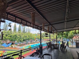 An outdoor seating area with tables and chairs, overlooking a pool and playground.