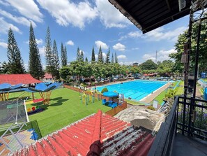 Una piscina con techo rojo, rodeada de árboles y un área verde con juegos infantiles.