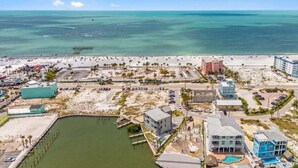 Une zone côtière comprenant une plage, un port de plaisance et plusieurs bâtiments, dont un hôtel avec une piscine.