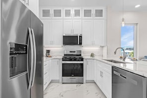 A modern kitchen with stainless steel appliances, white cabinetry, and a large window providing a view. - Luxury Lagoon Views, Pool & Steps to Beach Escape Near Times Square - Casa Laguna 3 - Roelens (Fort Myers Beach)