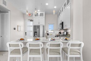 A modern kitchen with white cabinetry, a central island with seating, stainless steel appliances, and pendant lighting. - Luxury Lagoon Views, Pool & Steps to Beach Escape Near Times Square - Casa Laguna 3 - Roelens (Fort Myers Beach)