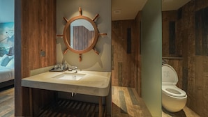 Ein Badezimmer mit Holzwaschtisch, einem runden Spiegel im Schiffsschrauben-Design, Toilette und Duschbereich.