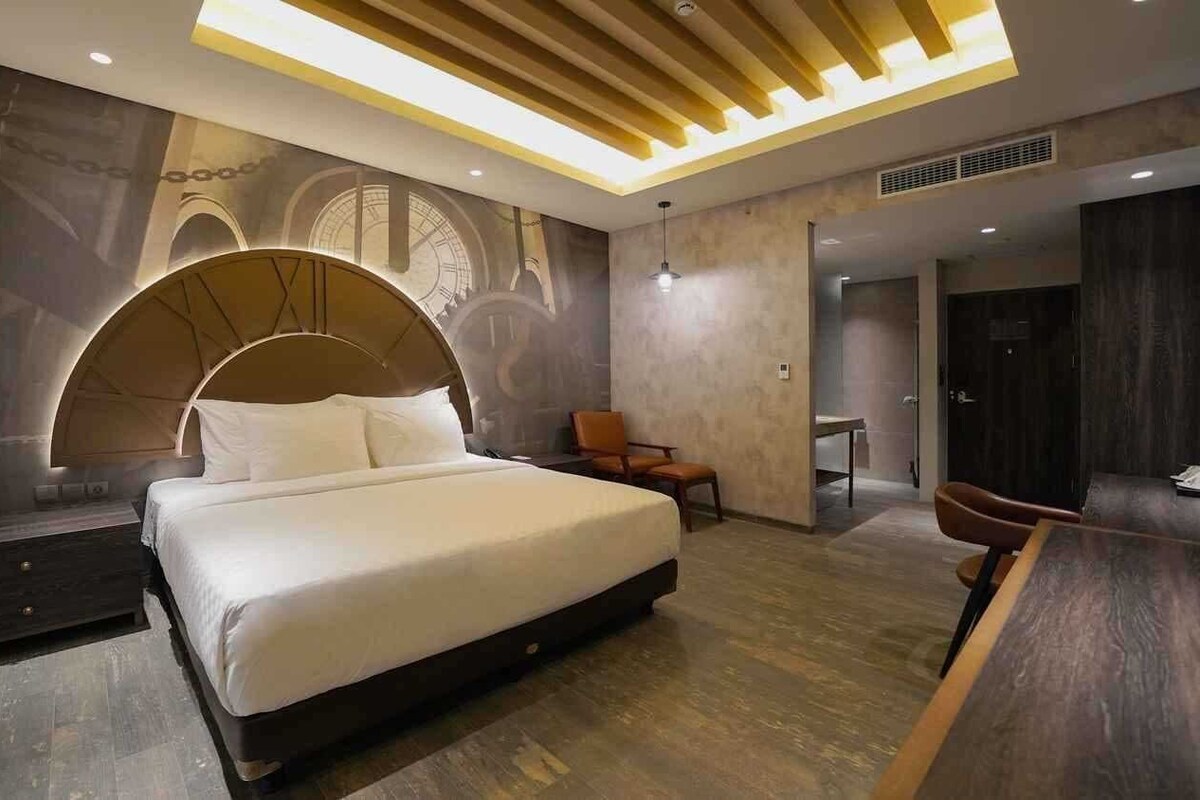 A modern hotel room with a large bed, a desk, and a chair.