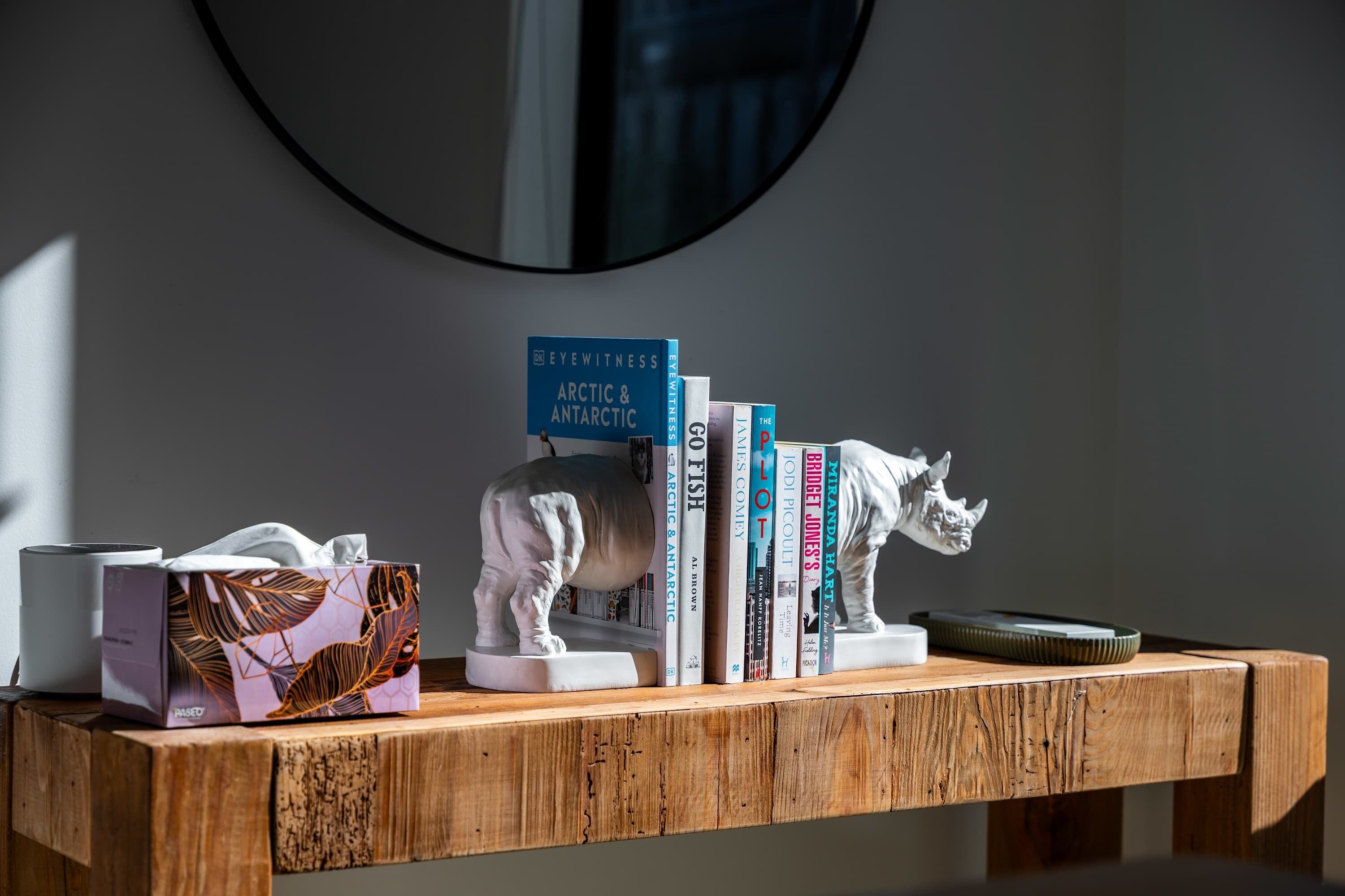 A wooden shelf with books, a tissue box, and a white sculpture.