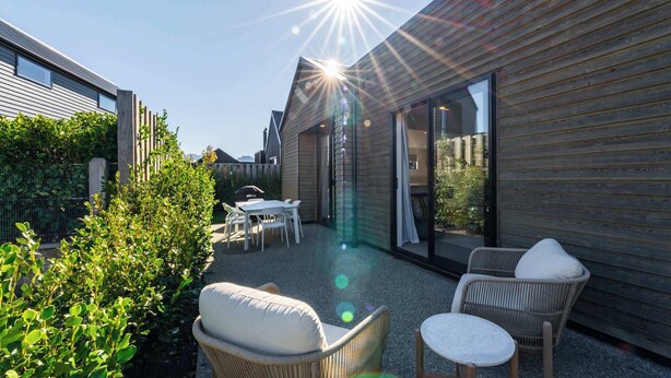 Un patio moderno al aire libre con mobiliario de mimbre, una mesa y un vidrio que da a un espacio cubierto.