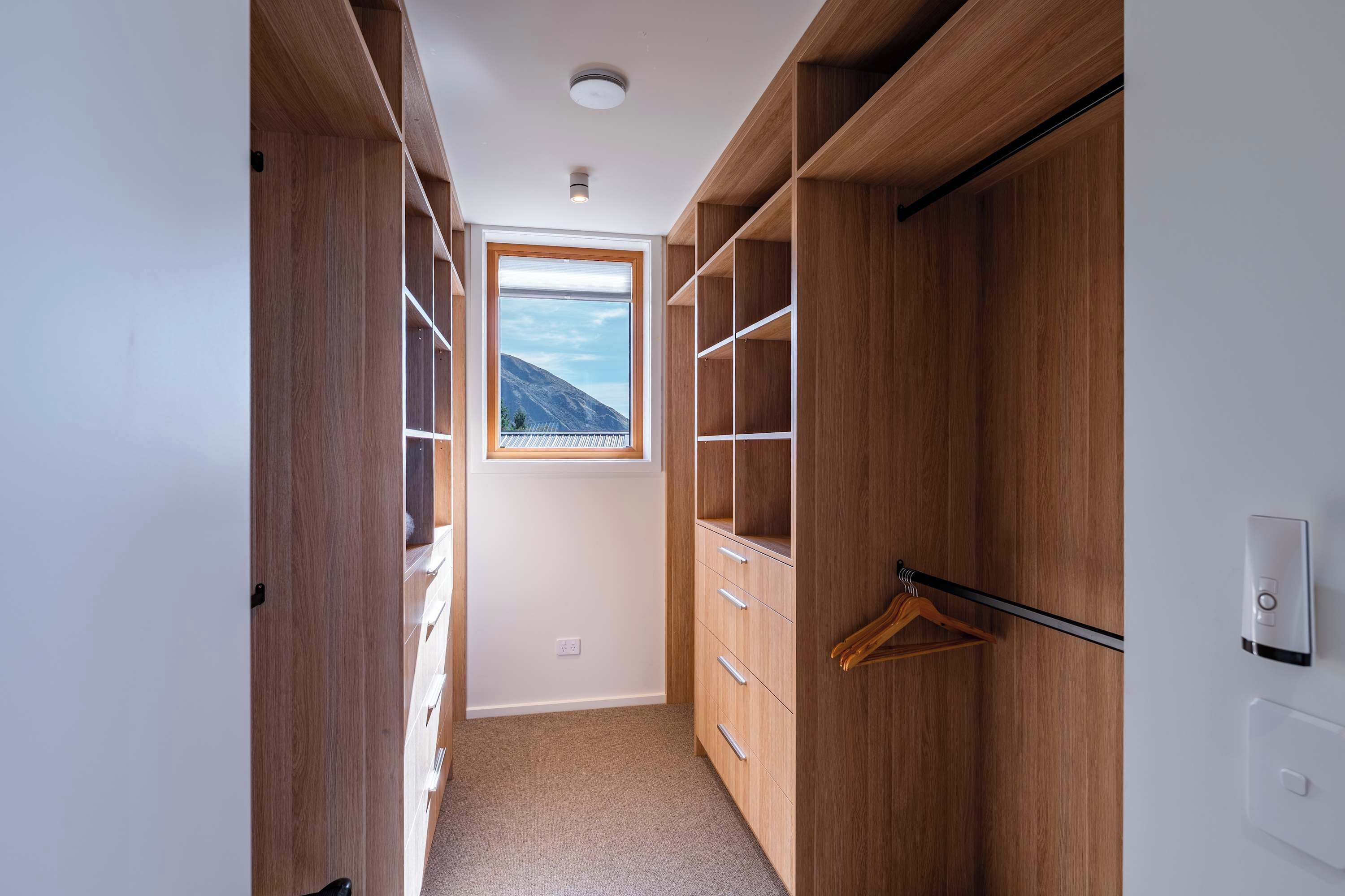 A narrow hallway with wooden shelving units, a window with a mountain view, and a hanging coat rack.