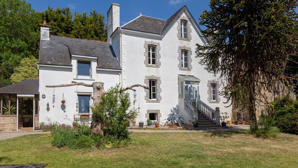 Ein zweistöckiges Haus mit Steinverkleidung, einer sichtbaren Treppe und einem Garten mit Kübelpflanzen.