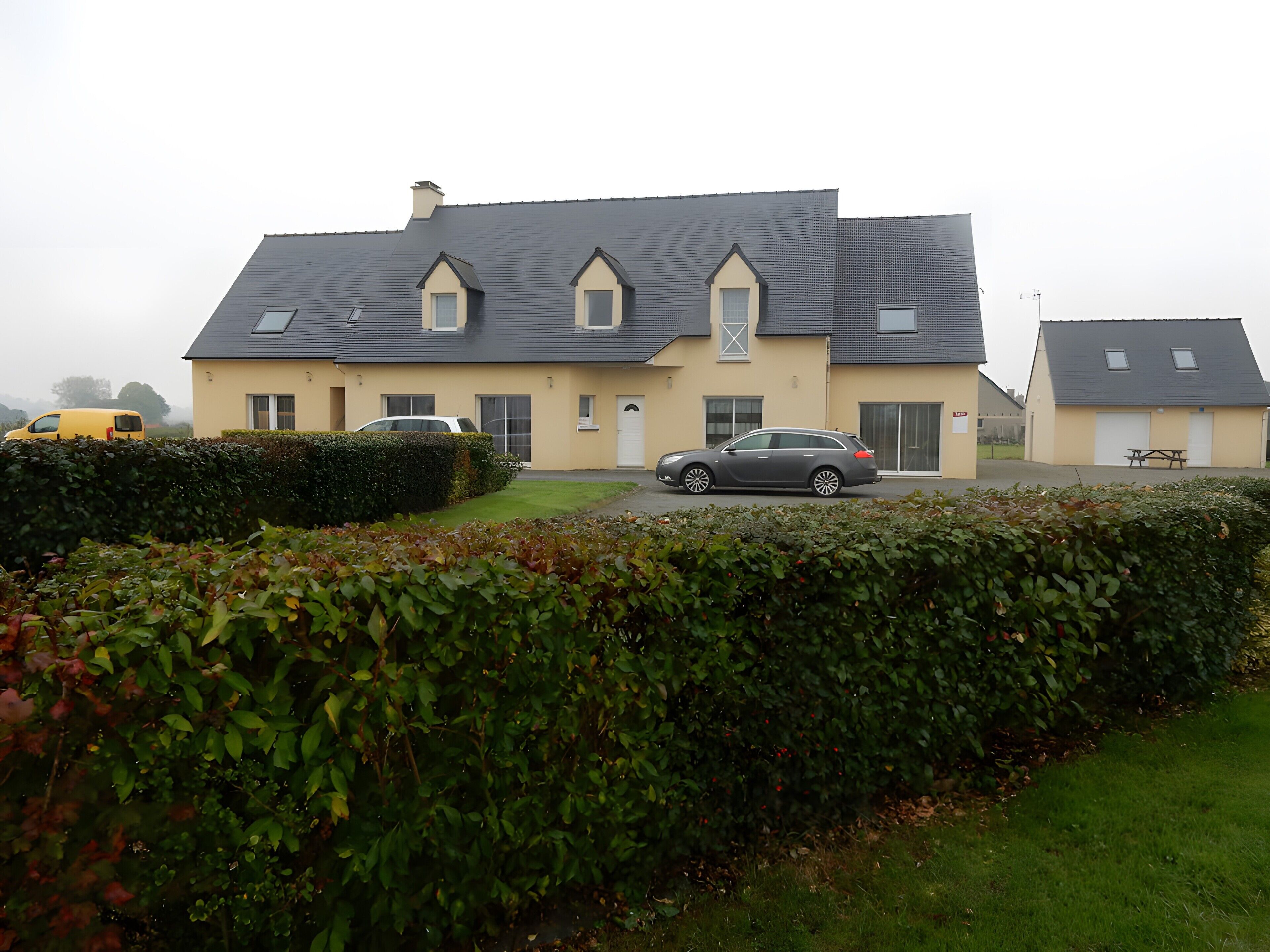 A residential house with a sloped roof, a garage, and a front yard with a hedge.
