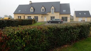 Une grande maison à deux étages, avec un toit gris, une allée et une voiture garée devant.