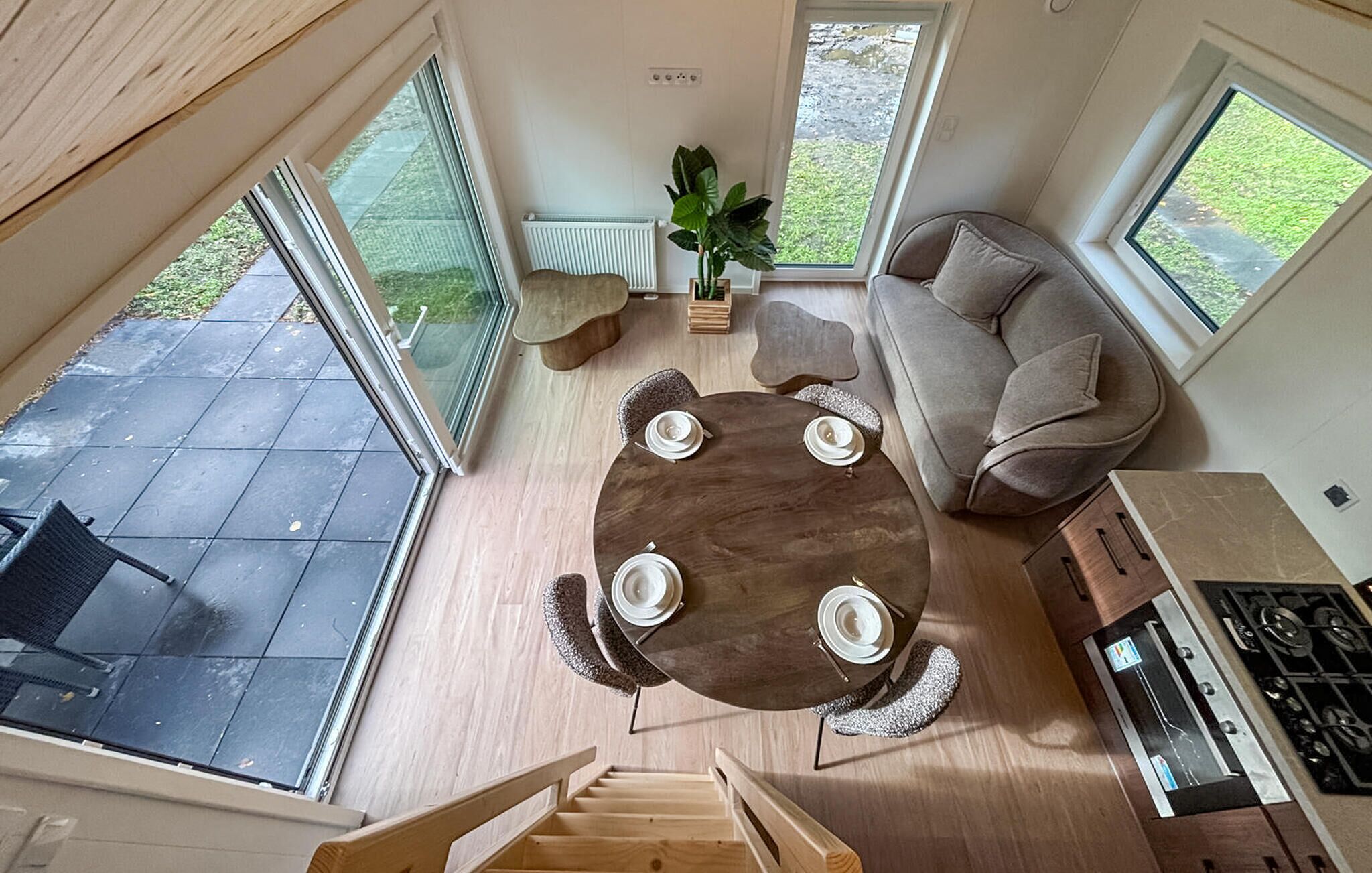 Een ruime woonkamer met een ronde houten tafel gedekt voor vier personen, een bank en een keuken met een fornuis.