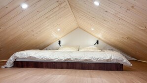 Ein Schlafzimmer mit schrägverdeckter Decke, Holzboden und einem Bett mit weißer Bettwäsche.