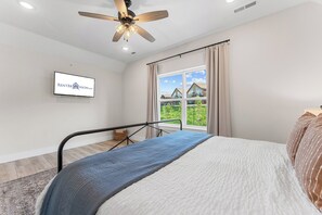 A bedroom with a bed, a ceiling fan, a television, and a window with a view of houses. - View of Outdoor Pool&Table Rock_Arcades_Pvt Hot Tub_Shuffleboard_Free Tickets (Kimberling City)