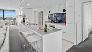 A modern kitchen with a central island, bar stools, and a view of the city. - Modern 2BR Oasis with Pools, Gym and Secure Parking (Surfers Paradise)