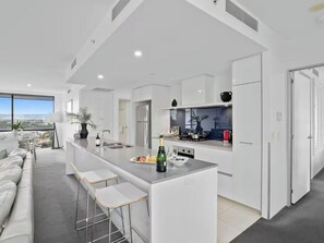 A modern kitchen with a central island, bar stools, and a view of the city. - Modern 2BR Oasis with Pools, Gym and Secure Parking (Surfers Paradise)