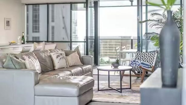 A modern living room with a sofa, a coffee table, and a balcony with outdoor furniture. - Modern 2BR Oasis with Pools, Gym and Secure Parking (Surfers Paradise)