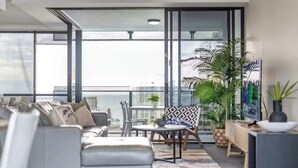 A modern living room with a sofa, chairs, a small table, and potted plants. - Modern 2BR Oasis with Pools, Gym and Secure Parking (Surfers Paradise)