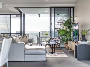 A modern living room with a sofa, chairs, a small table, and potted plants. - Modern 2BR Oasis with Pools, Gym and Secure Parking (Surfers Paradise)