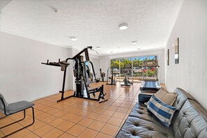 A spacious room with a gym area, a couch, and a view of the outdoors. - Comfy 1BR + Free Parking |  Stroll to Parklands (Southport)