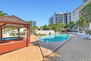 A swimming pool with lounge chairs and a gazebo, surrounded by palm trees and modern buildings. - Comfy 1BR + Free Parking |  Stroll to Parklands (Southport)