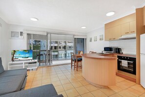 A modern kitchen with a wooden island, a dining area with a table and chairs, and a living room with a sofa and a TV. - Comfy 1BR + Free Parking |  Stroll to Parklands (Southport)