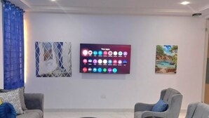 Uma sala de estar moderna com uma TV de tela plana, sofás cinzas, uma mesa de centro e almofadas decorativas.