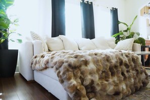 A living room with a sofa, a fur throw, and a potted plant. - The Healing Pad. Sleeps 6,Walk to Beach, Perfect for Small Retreats & Groups (Galveston)