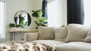 Sala de estar com sofá, espelho redondo, planta em vaso e manta aconchegante.