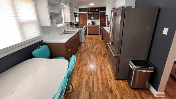 Una cocina moderna con refrigerador de acero inoxidable, armarios de madera, lavadora integrada y una ventana con persianas.