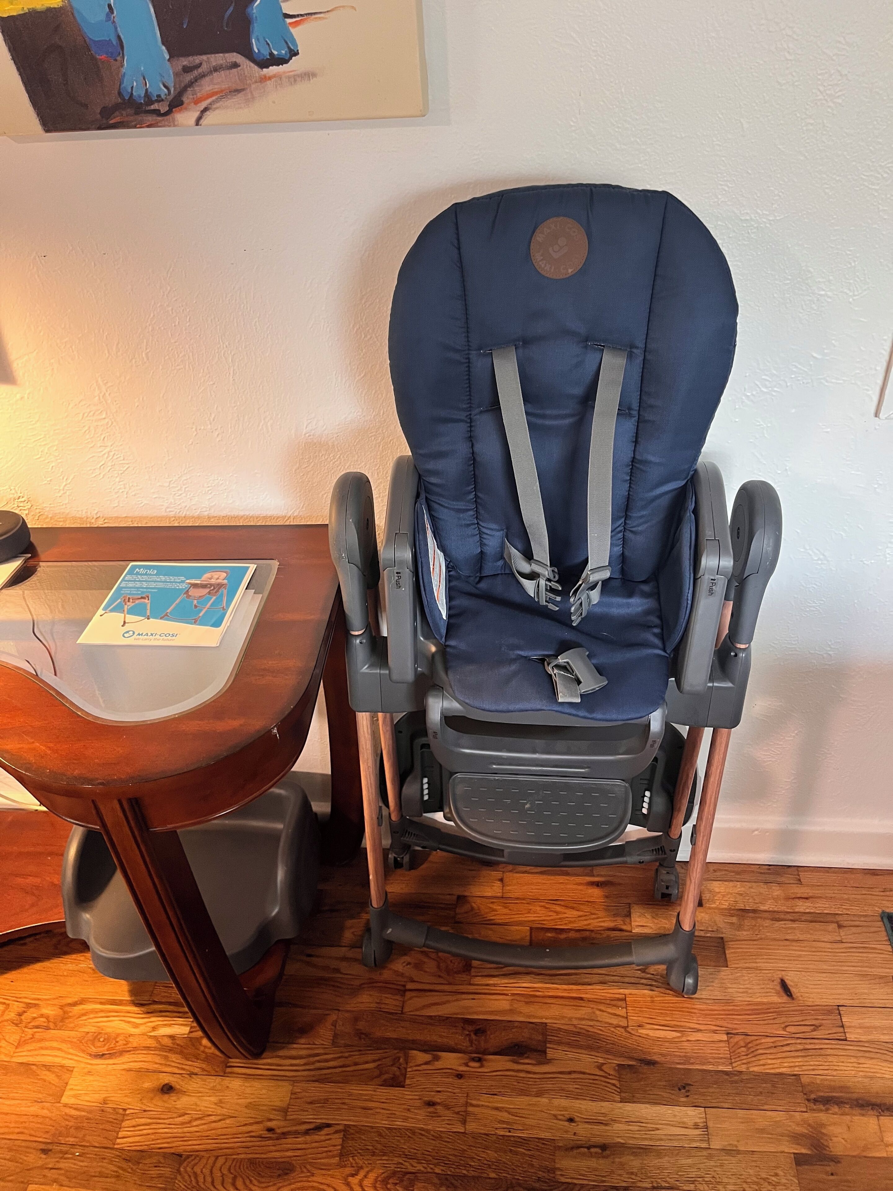 Um balanço azul para bebê com apoio para os pés e uma mesinha lateral com um folheto.