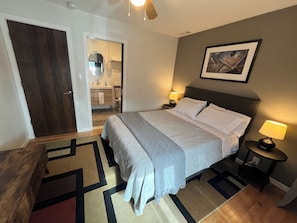 A hotel room with a bed, bedside tables, a nightstand, a door, a bathroom visible through an open door, and a framed picture on the wall. - Superb 5-bedroom house with AC in friendly Fort Collins (Fort Collins)