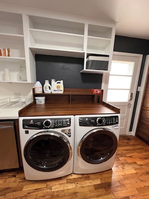 A laundry area with two front-loading washing machines, a countertop with detergent bottles, and a white shelving unit above. - Superb 5-bedroom house with AC in friendly Fort Collins (Fort Collins)