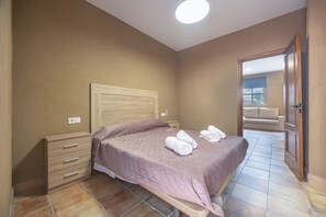 A bedroom with a bed, bedside tables, a wooden headboard, and a view of a balcony.
