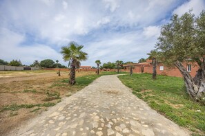 A paved pathway leading to a building with a red facade, surrounded by greenery and palm trees. - Hacienda El Legado 4 Apartment with Shared Pool, Wi-Fi & Air Conditioning (Chiclana de la Frontera)