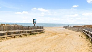 Un sentier de plage sablonneux, bordé de clôtures en bois et agrémenté d’un panneau indicateur.