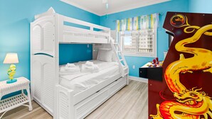 Une chambre avec un lit superposé, un ventilateur de plafond, une fenêtre avec des rideaux et une œuvre d’art sur le thème des dragons accrochée au mur.