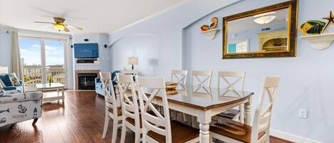 A dining area with a wooden table and white chairs, a ceiling fan, and a large window with a view.
